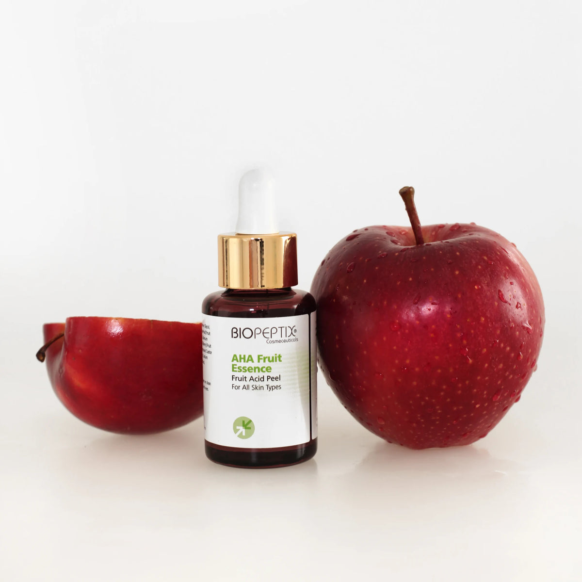סרום חומצת פירות AHA Fruit Essence של Biopeptix, בקבוק טפטפת לצד תפוח אדום וחצי תפוח